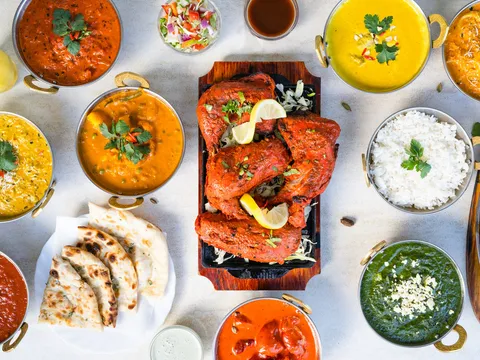 An overhead spread of Indian dishes at Nizami Biryani & Grill in Agoura Hills, California — a sizzler of tandoori chicken surrounded by curries in copper karahis, basmati rice, naan and saag