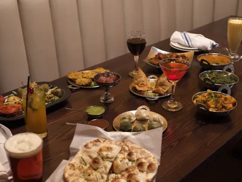 Table spread of curries, momos, tandoori chicken, naan and drinks in a booth at Saffron Indian Grill