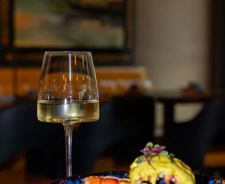 Plated lobster dish with a saffron-yellow sauce in a blue bowl, served beside a glass of white wine at Rivayat Creative Indian in Charleston