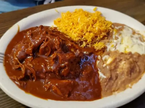 Plate of chicken mole with Spanish rice and refried beans topped with melted cheese at Kiki's Mexican Restaurant in El Paso