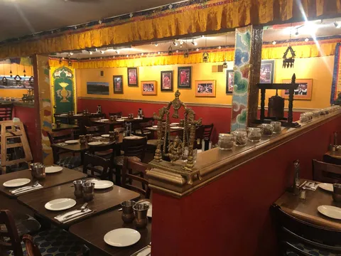 Dining room at Annapurna Cafe, with red walls, framed photographs, a brass shrine and set tables