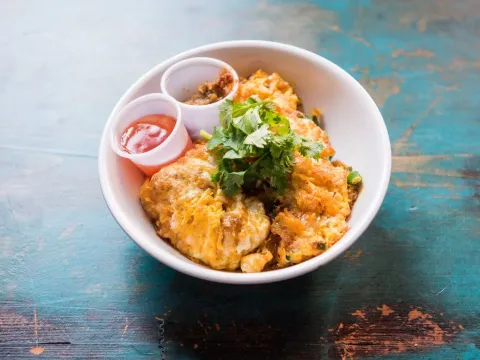 Oh Chien pan-fried oyster omelette topped with cilantro, served with chili sauces at Kopitiam