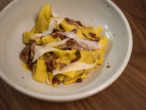 A bowl of pappardelle pasta with shaved cheese at Fairchild