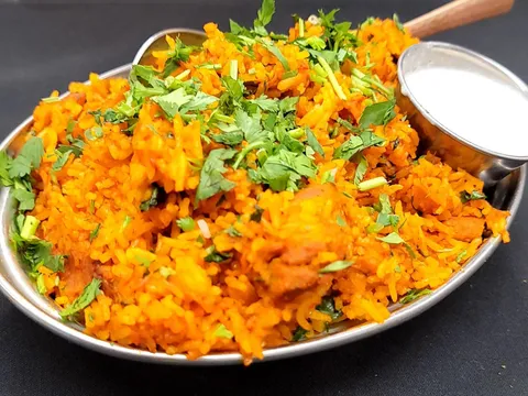 Chicken biryani topped with cilantro and served with a cup of raita in a steel dish at Little India Restaurant & Bar in Denver