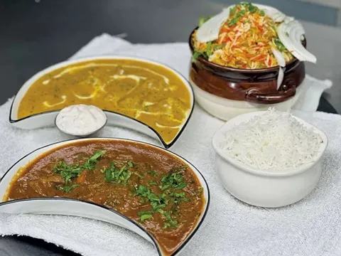 Indian spread at Tikka House in Winooski — a dark curry and a lighter curry in crescent bowls, raita, a pot of chicken biryani and a bowl of basmati rice