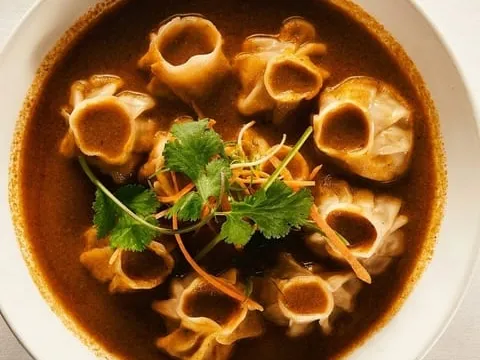 Overhead view of Nepalese dumplings in a dark, rich sauce garnished with cilantro and shredded carrots