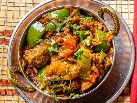 A karahi of India's Restaurant lamb bhoona with green and red bell peppers and cilantro in a copper-handled bowl