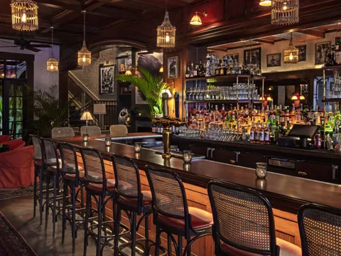 The warmly lit wood bar and lounge at Le Colonial Chicago with birdcage lanterns, cane bar stools and tropical decor