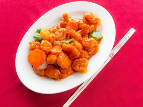 General Tso's chicken — battered chicken pieces in glossy orange chili sauce with green bell pepper and a carved carrot garnish on a white oval plate with chopsticks, at Kung Fu Thai & Chinese Restaurant in Las Vegas