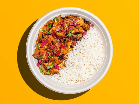 Chicken tikka masala with basmati rice in a round bowl on a bright yellow background