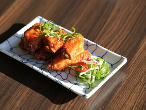 A plate of Dumpling Time's glazed crispy fried chicken topped with scallion curls, on a blue net-patterned plate
