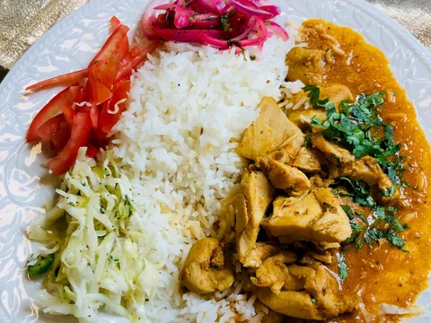 Chicken curry over basmati rice with cabbage slaw, sliced tomato and pickled red onions on a white plate at Klay Oven Kitchen