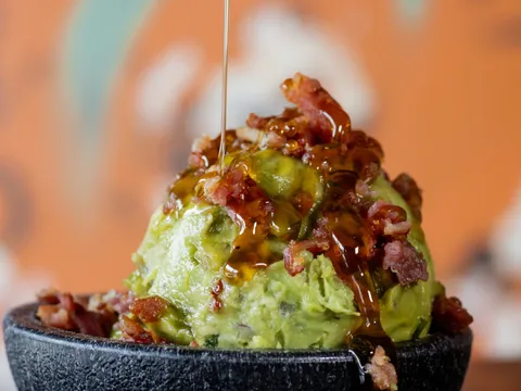 Guacamole in a stone molcajete topped with bacon and drizzled with hot honey at Barrio Tacos