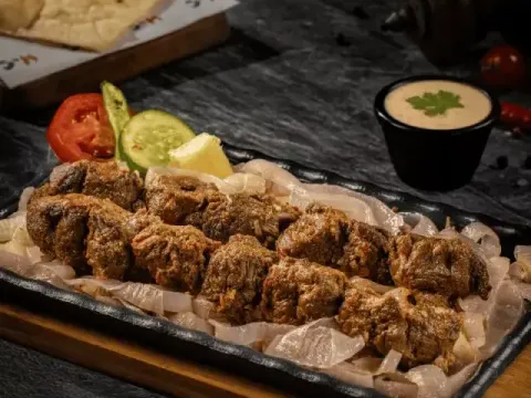 Grilled beef boti skewers served over onions on a sizzling platter with naan at Kababjees.