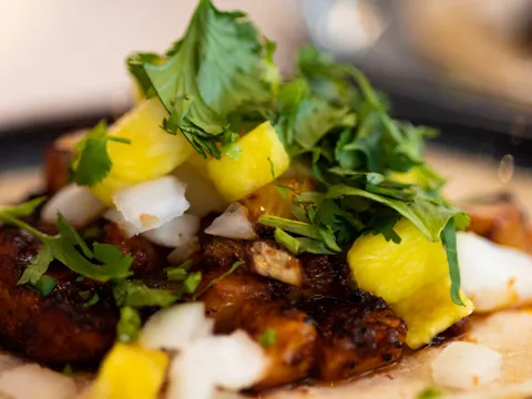 A Taco Luchador al pastor taco on a corn tortilla topped with grilled pineapple, white onion and cilantro