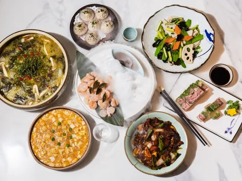 Overhead spread of Shanghainese dishes at CheLi including a steamer of soup dumplings, crab-meat tofu stew, poached shrimp and lotus-root stir-fry