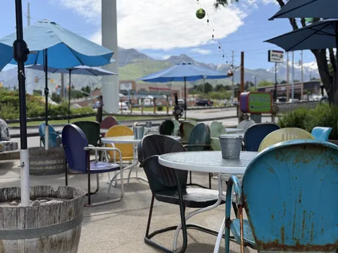 The patio at Lone Star Taqueria in Cottonwood Heights: colorful vintage metal chairs and umbrella-shaded tables with the Wasatch mountains in the background
