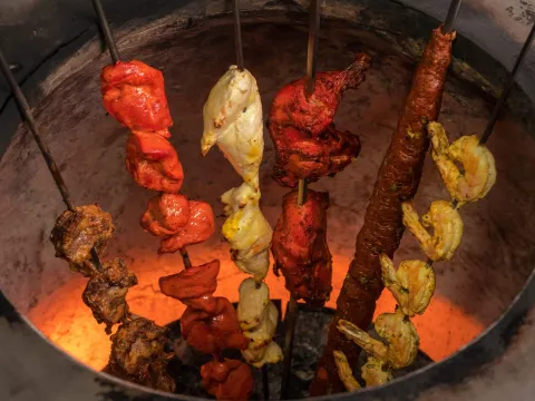 Assorted tandoori kebabs, chicken and shrimp on skewers cooking inside the glowing tandoor oven at Chola in New York