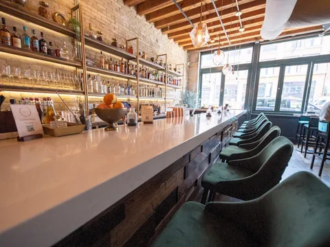 Long bar with green stools and a lit back bar at Saffron in Milwaukee's Third Ward