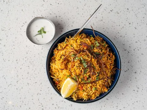 Bowl of biryani with lemon and raita, seen from above, at Tabla