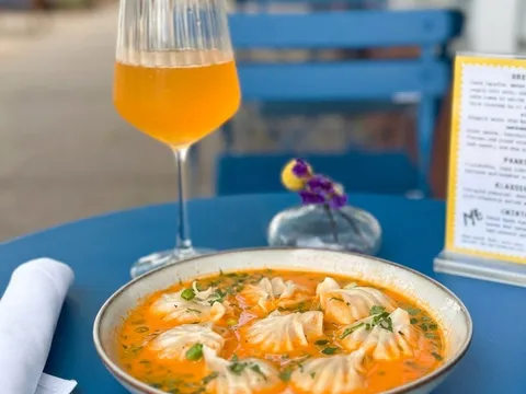 Jhol momo — steamed dumplings in a spiced tomato broth — served with a drink on an outdoor table at Makalu Boston