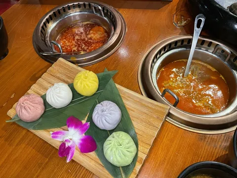 Colorful assorted soup dumplings on a wooden board beside two copper hot pot broths at Chubby Cattle