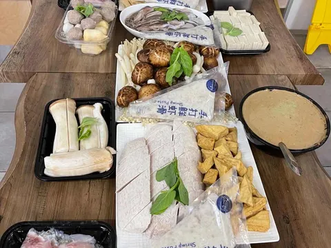 Overhead spread of fresh hot pot ingredients — mushrooms, tofu, sliced meats, prawns, scallops and shrimp paste — on a wood table at Xi'an Noodles