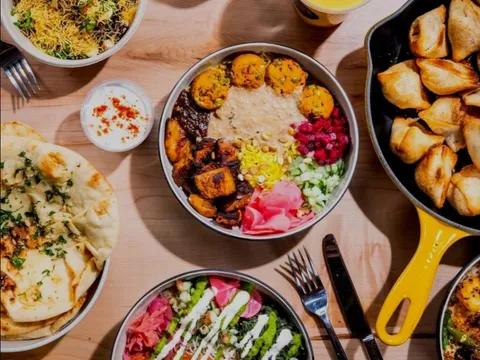 Overhead spread of RASA bowls, naan, samosas, raita, and colorful drinks on a wood table