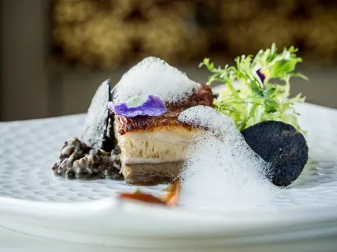 Plated crispy pork belly starter with black-lentil, herb foam and greens at All Spice, San Mateo