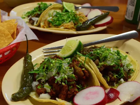 Two plates of street tacos at Taqueria La Guadalupana topped with chopped onion and cilantro, served with grilled jalapeños, radishes, lime and a basket of tortilla chips