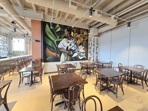 Dining room at Santoro in Omaha, with wooden bentwood chairs and tables and a large mural of a woman holding calla lilies on the wall