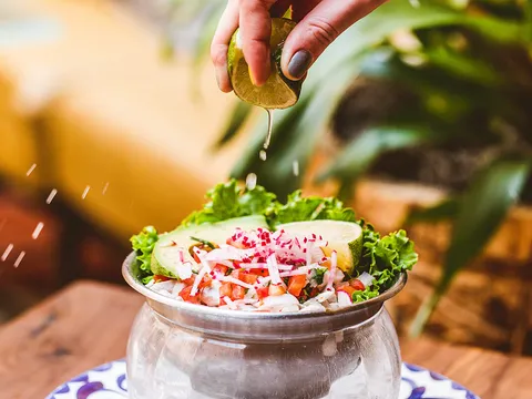 Lime being squeezed over a bowl of ceviche with radish, avocado and tomato at Fonda San Miguel