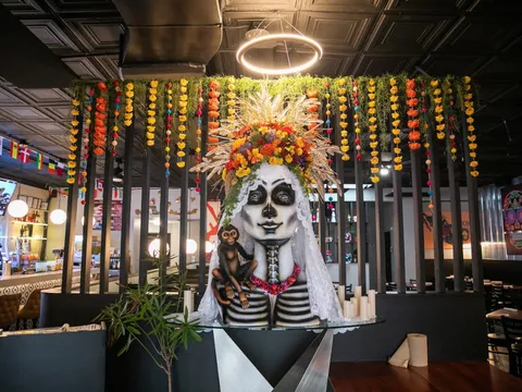 The dining room at Blue Habanero in Richmond, with a large Catrina sculpture in a marigold flower crown beneath hanging garlands