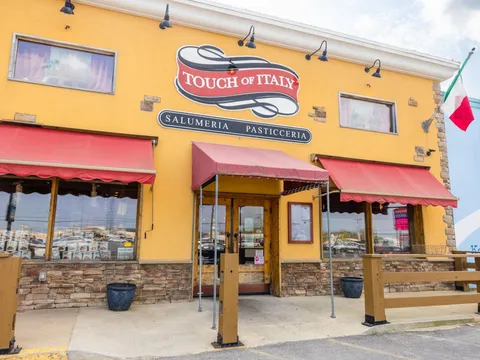 Yellow stucco storefront of Touch of Italy with red awnings over the salumeria and pasticceria windows