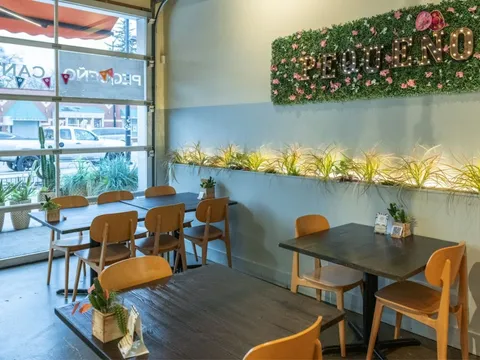 The dining room at Pequeño Cantina, with wooden tables and chairs beneath an illuminated "PEQUEÑO" marquee sign set into a greenery wall