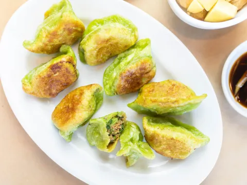 Plate of Katy's Dumplings pan-fried green (vegetable-dough) dumplings with soy dipping sauce