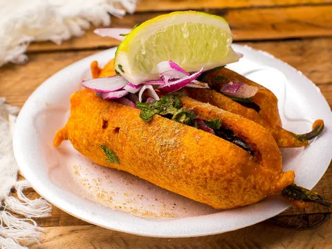 Mirchi bajji, a batter-fried chilli fritter topped with sliced red onion and a lime wedge on a plate, at Bawarchi Biryanis in Sandy Springs, Georgia