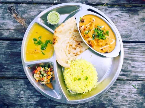 A Zareen's thali with chicken tikka masala, tarka daal, chopped salad and green chutney, naan and saffron rice on a steel platter