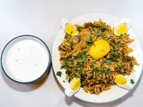 Plate of biryani with boiled egg and a bowl of raita at Mirch Masala