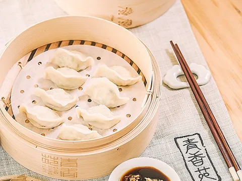 Steamed Qing Xiang Yuan dumplings in a bamboo steamer with dipping sauce and the restaurant's branded linen
