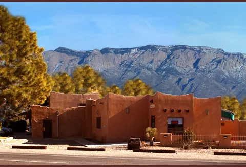 Exterior of the adobe Casa de Benavidez restaurant with its sign, set against the Sandia Mountains in Albuquerque, New Mexico