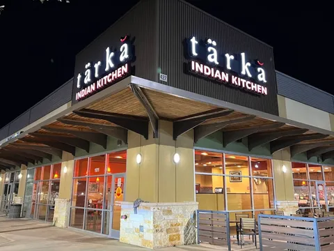 Exterior storefront of Tarka Indian Kitchen at its Stone Oak location in San Antonio at night, with the illuminated tarka Indian Kitchen sign above the entrance