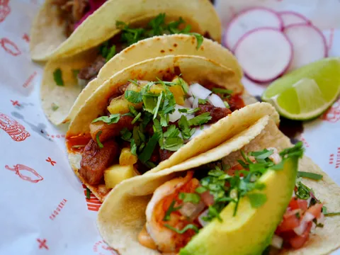 Three tacos with cilantro, onion, pineapple, avocado and shrimp on Taqueria Habanero branded paper, with lime and radish, at Taqueria Habanero in Washington, DC