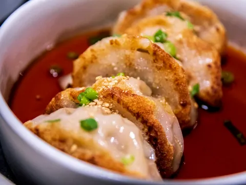 Pan-fried pork and kimchi mandu dumplings in chili sauce topped with scallions and sesame at Anju