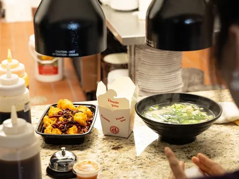 Dishes at Ping's Sichuan Kitchen on the service counter in San Antonio — a plate of dry-fried chili bites, a takeout box, and a steaming bowl of soup beside squeeze bottles of sauce