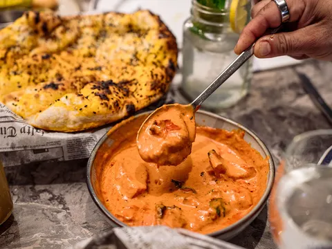 A spoon lifting creamy butter-chicken-style curry from a steel bowl, with charred garlic naan alongside, from Bombay Blue Indian Bistro in Edison, New Jersey
