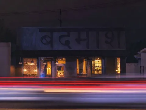 Badmaash DTLA storefront illuminated at night with traffic lights passing in front