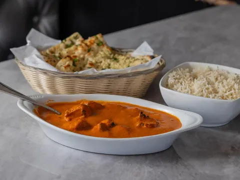 Asiana Indian Cuisine chicken tikka masala in a white dish served with a basket of garlic naan and a bowl of basmati rice