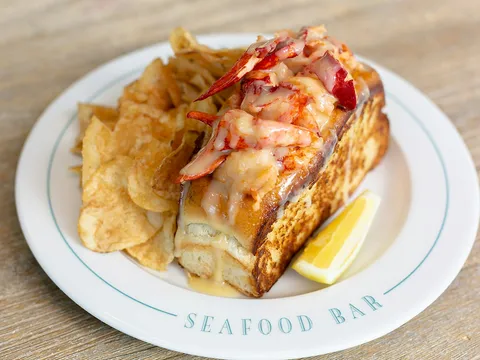 Warm New England lobster roll on a buttered split-top bun with potato chips and lemon on a Saltie Girl Seafood Bar plate
