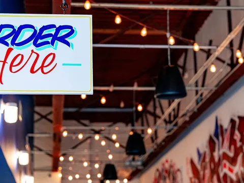 Colorful interior of El Malo Tacos in Charlotte with a 'TACOS' sign and 'Mercado' shelves, papel picado banners overhead, and red chairs at white tables